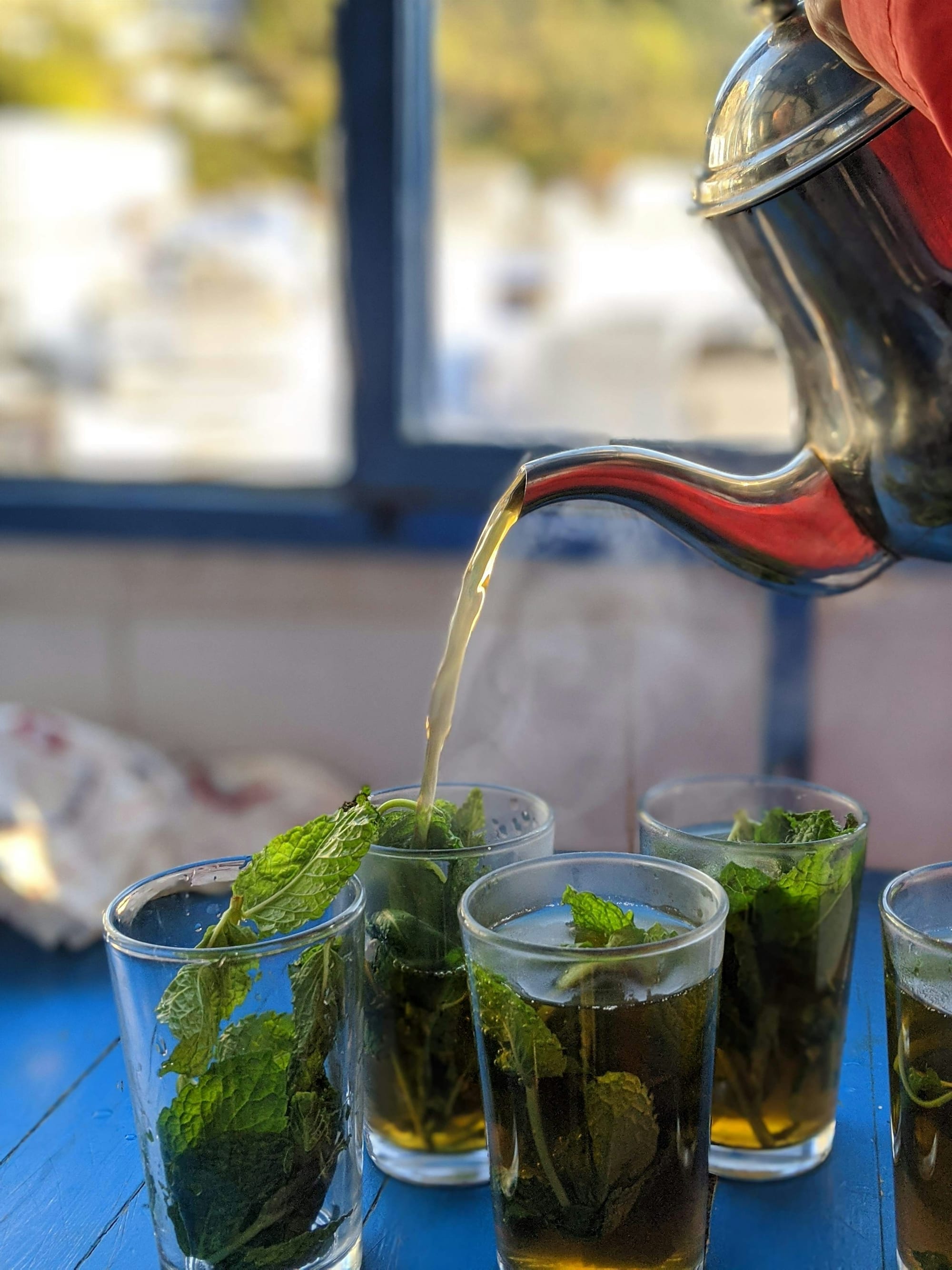 Thé à la menthe versé de haut dans un verre garni de menthe fraîche